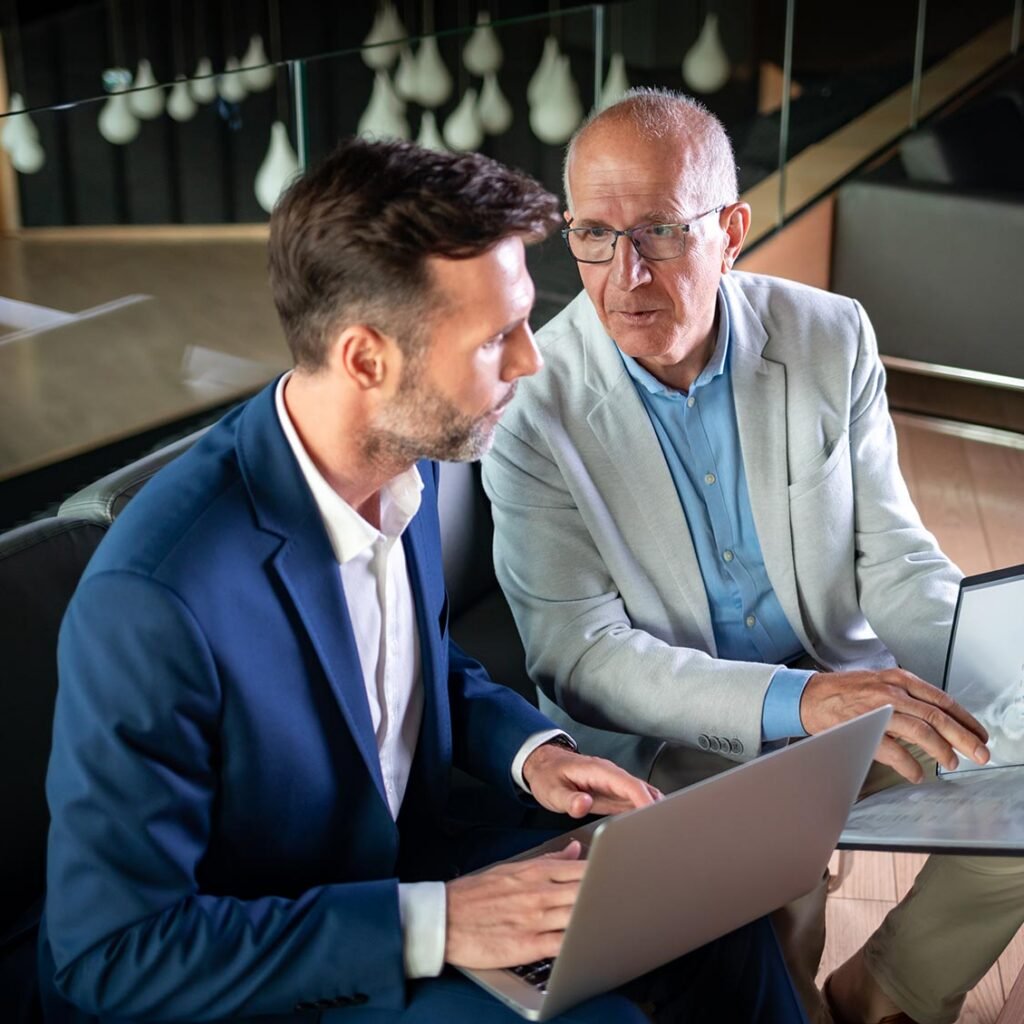 Dois homens a conversar junto a um computador analisando papéis para projetos de websites, com foco em preços, num escritório moderno