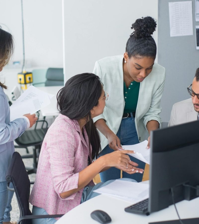 Equipa diversificada a participar numa discussão animada sobre websites para a página “Sobre Nós” num escritório moderno, promovendo colaboração e trabalho em equipa